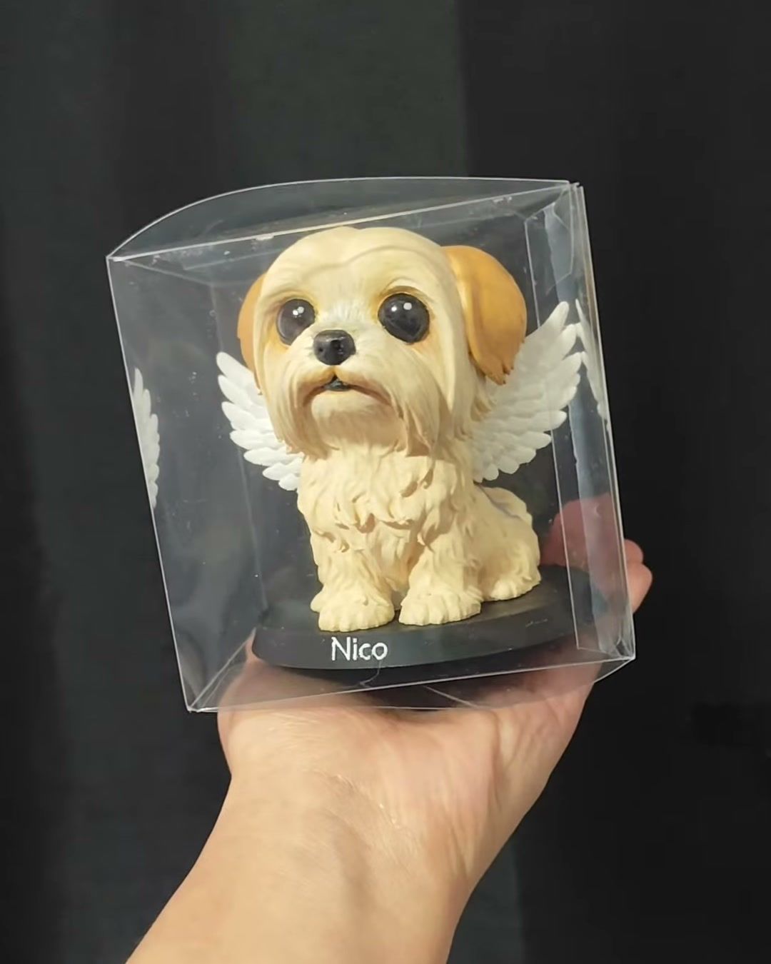 Figura de un perrito con alas dentro de su caja transparente, lista para entregar.