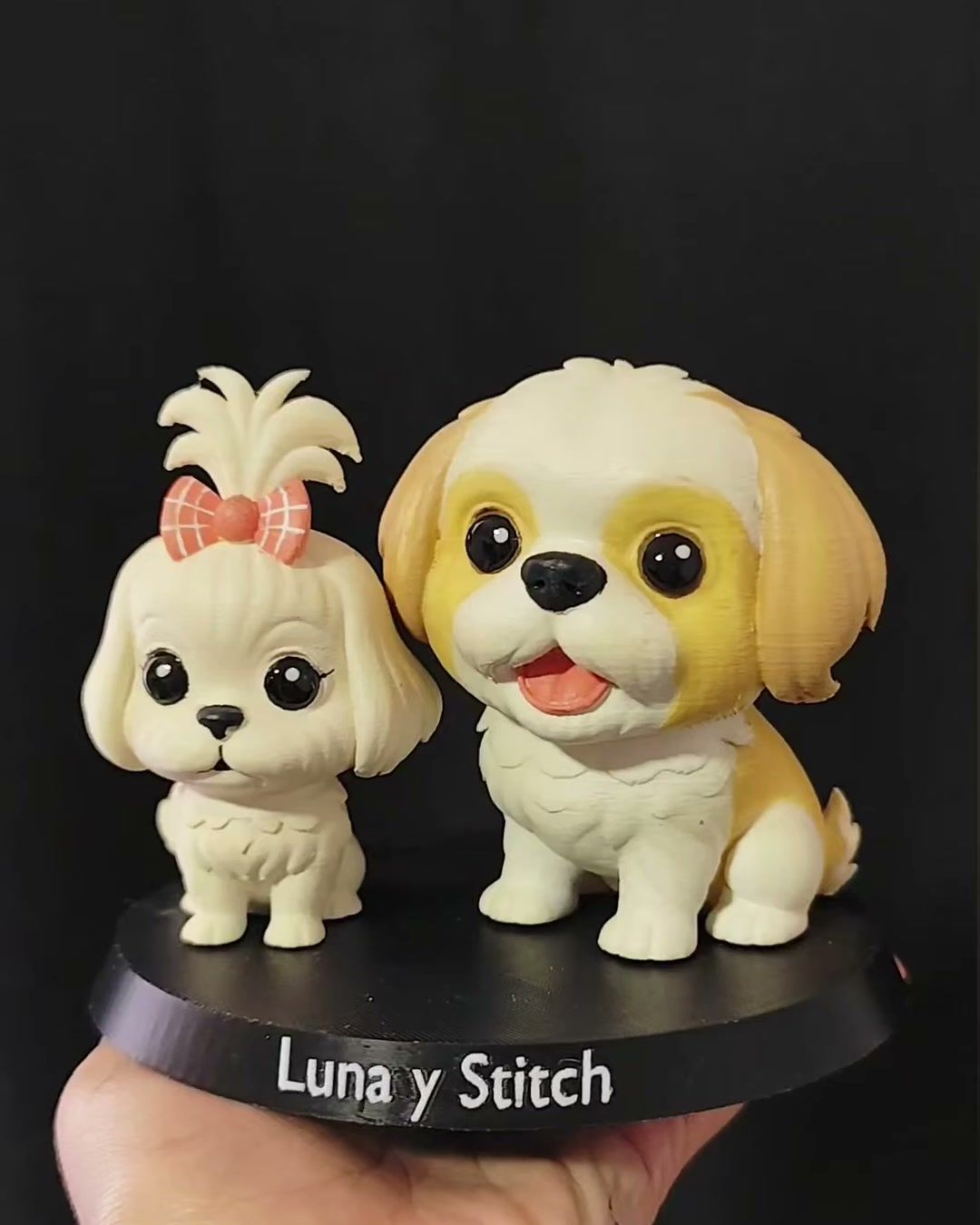 Dos figuras de perritos de pelo largo color crema, una con moño rosado, sobre base negra con los nombres Luna y Stitch.