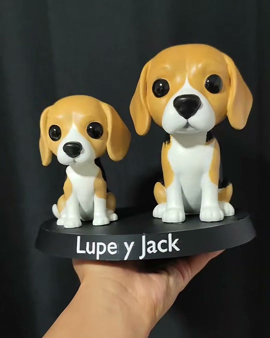 Dos figuras de perros beagle tricolor sobre una misma base negra con los nombres Lupe y Jack.