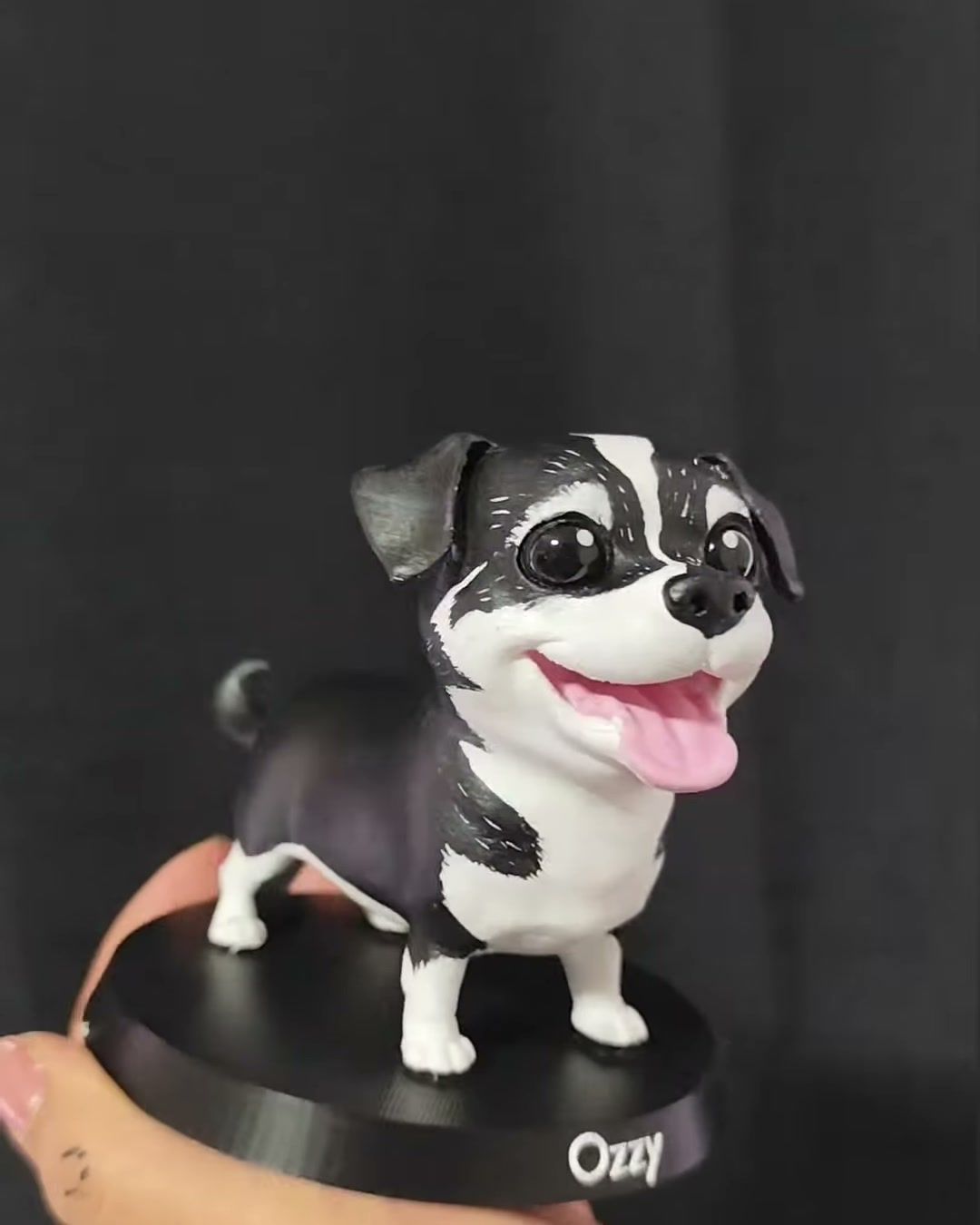 Figura de perro blanco y negro con la lengua afuera, de pie sobre base negra con el nombre Ozzy.