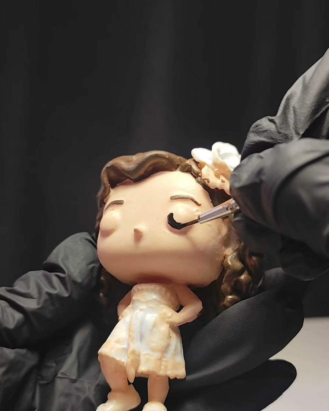 Mano con guante pintando con pincel los ojos de una figura de niña.