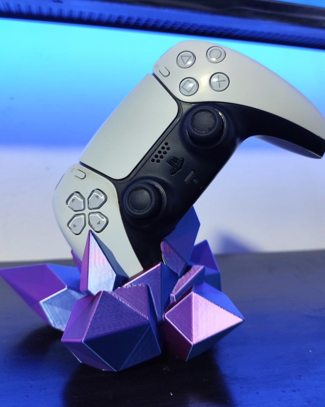 Soporte de cristales morados y azules que sostiene un control de videojuegos blanco, sobre un escritorio.